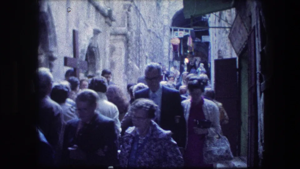 Crowded Jerusalem stone alley near the Garden Tomb, with tourists and pedestrians walking beneath awnings in a 1976 home-movie frame.