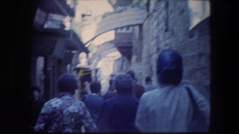 Tourist-shot 1976 Jerusalem alley view with pedestrians moving away under arched stonework and awnings.