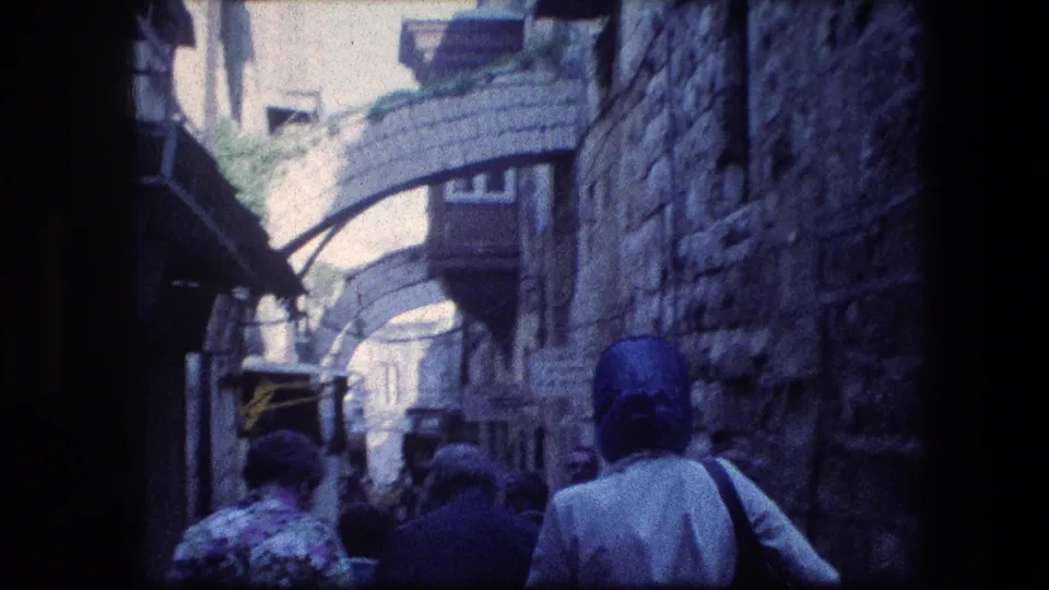 1976 8mm Jerusalem alley frame with tourists walking away between weathered stone walls and overhead arches.