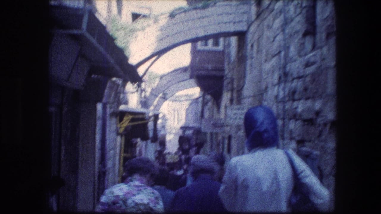 Crowd walking through a narrow stone alley beneath arched passages.