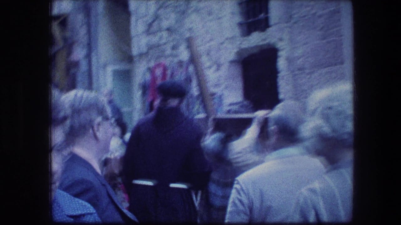 People gather near stone walls as a robed figure carries a wooden cross.