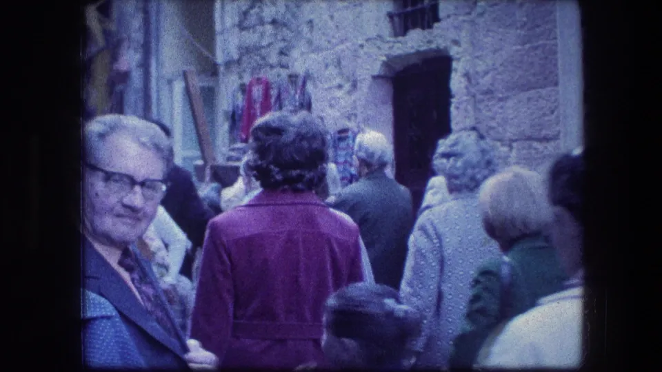 1976 Jerusalem frame showing a compact crowd in a stone alley, with a wooden cross partly visible above people in period clothing.