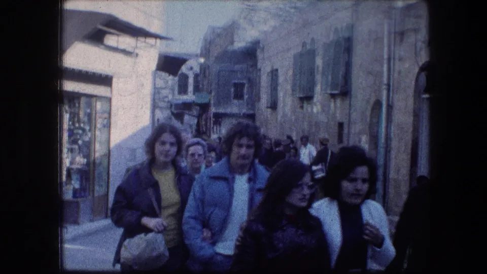 Adults in 1970s clothing walk toward the camera on a crowded Jerusalem street near the Garden Tomb.