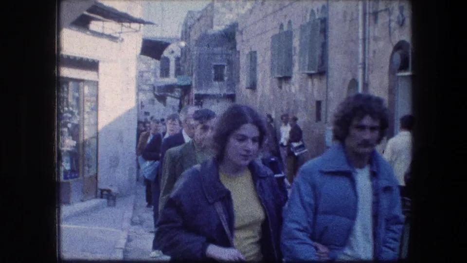 A woman and man in 1970s clothing walk arm in arm through a crowded street near Jerusalem's Garden Tomb.
