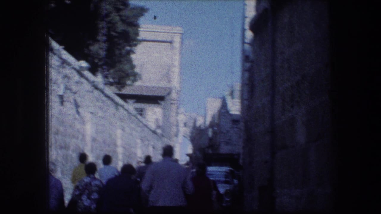 Tourists walk away through a narrow stone street in bright sun and shadow.
