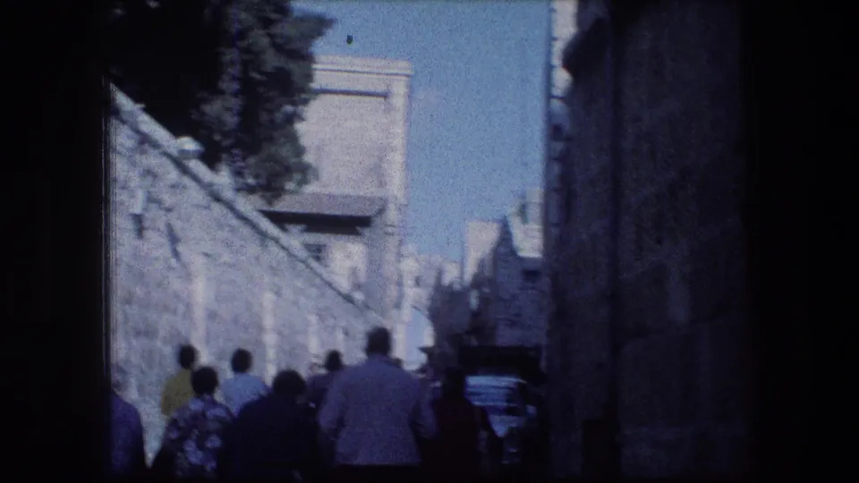 1976 8mm frame of tourists walking away through a narrow stone street near the Garden Tomb area in Jerusalem.