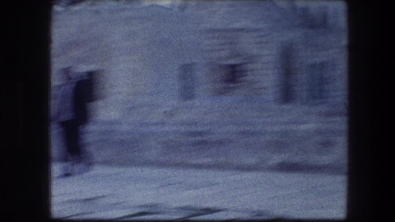 A blurred figure walks near a stone wall and arched opening.