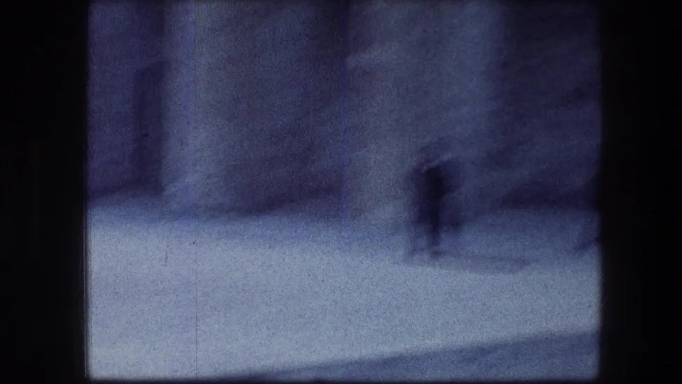 Soft, blue-tinted 8mm frame from Jerusalem with a distant blurred figure and indistinct stone architecture.