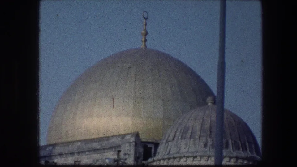 1976 8mm view of the Dome of the Rock area in Jerusalem, with a gold dome and smaller roof framed by dark foreground divisions.