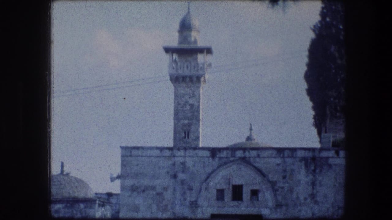 1976 8mm Jerusalem view of a minaret-like tower rising over stone walls, with a dome partly visible and a dark tree at right.