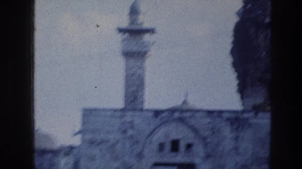Soft 1976 8mm Jerusalem frame with blue tint, showing stone architecture, an arched front and a tower partly obscured by blur.