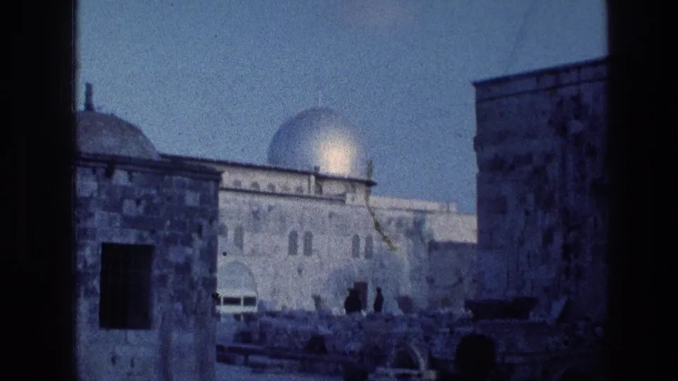 1976 8mm Jerusalem frame showing domed stone architecture and small silhouetted visitors near foreground masonry.