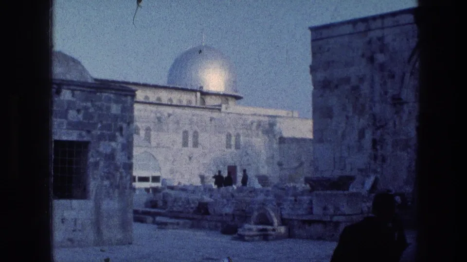 1976 8mm view in Jerusalem showing the Dome of the Rock beyond stone courtyard architecture, framed by a dark vertical opening with small silhouetted visitors.