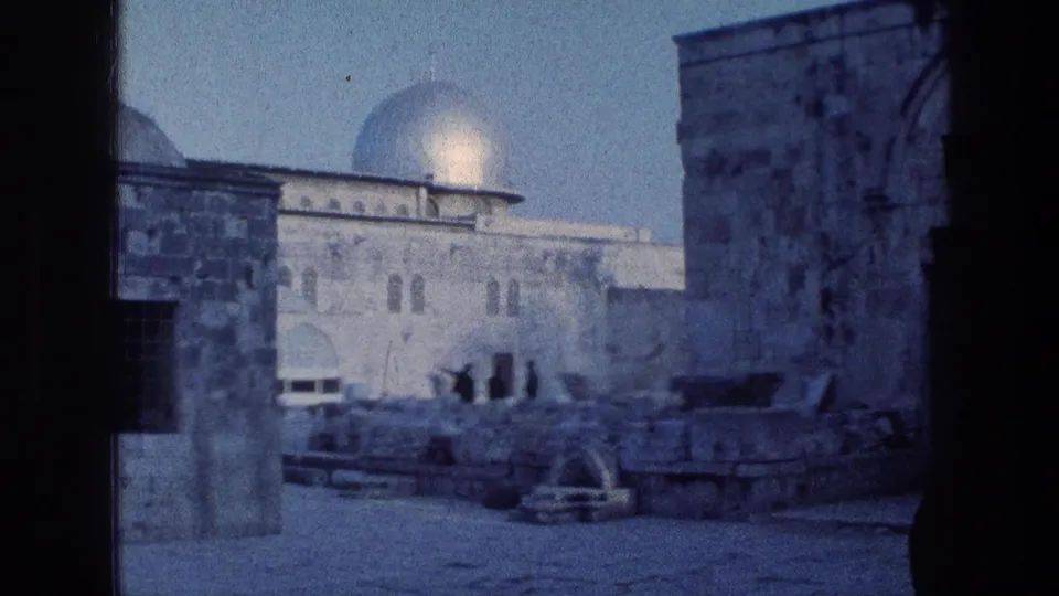 1976 8mm Jerusalem frame with the Dome of the Rock and surrounding stone architecture viewed through dark foreground columns, with small figures in the courtyard.