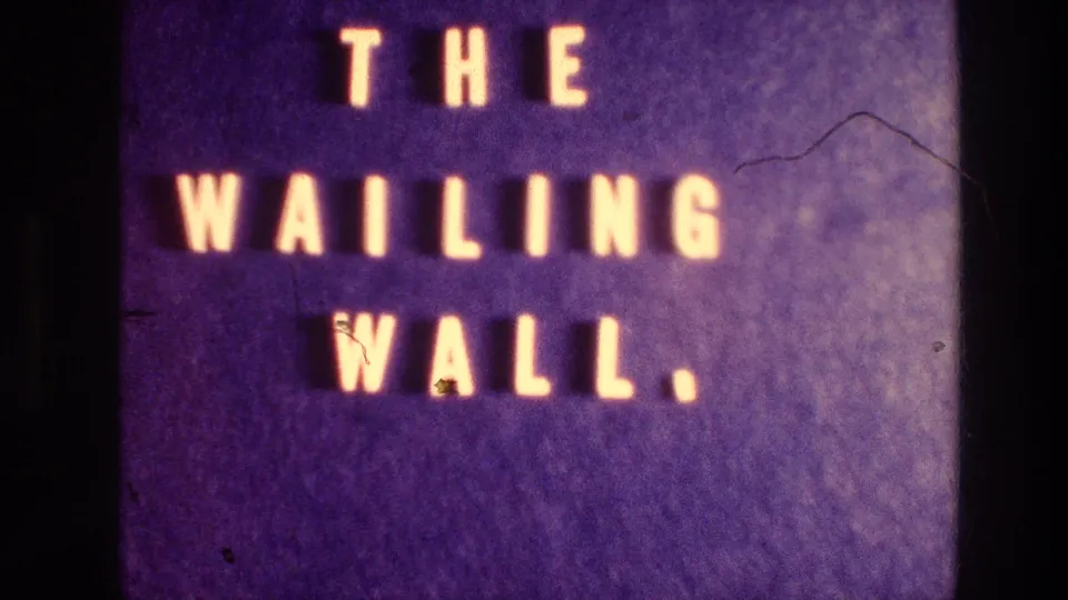 1976 home-movie title card on purple background with glowing yellow lettering reading THE WAILING WALL, filmed with visible 8mm grain and scratches.