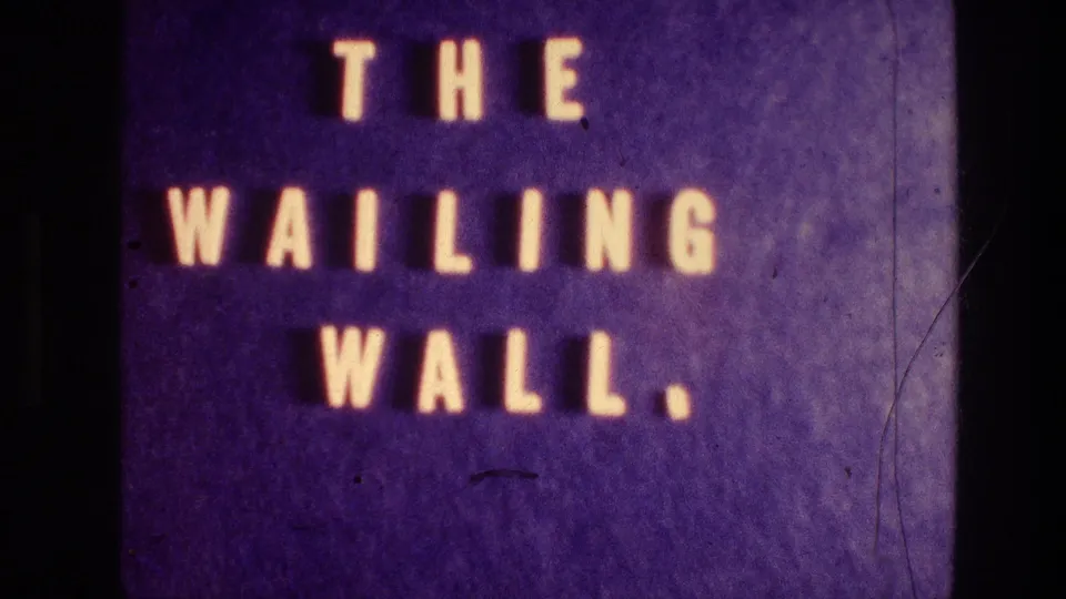 Soft 8mm frame of the Wailing Wall title card, with large glowing letters and visible film scratches.