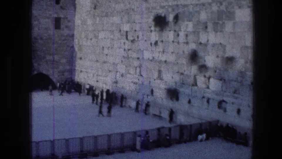 1976 8mm view of visitors gathered near a weathered stone wall at a Jerusalem religious site, seen from a distant home-movie angle.