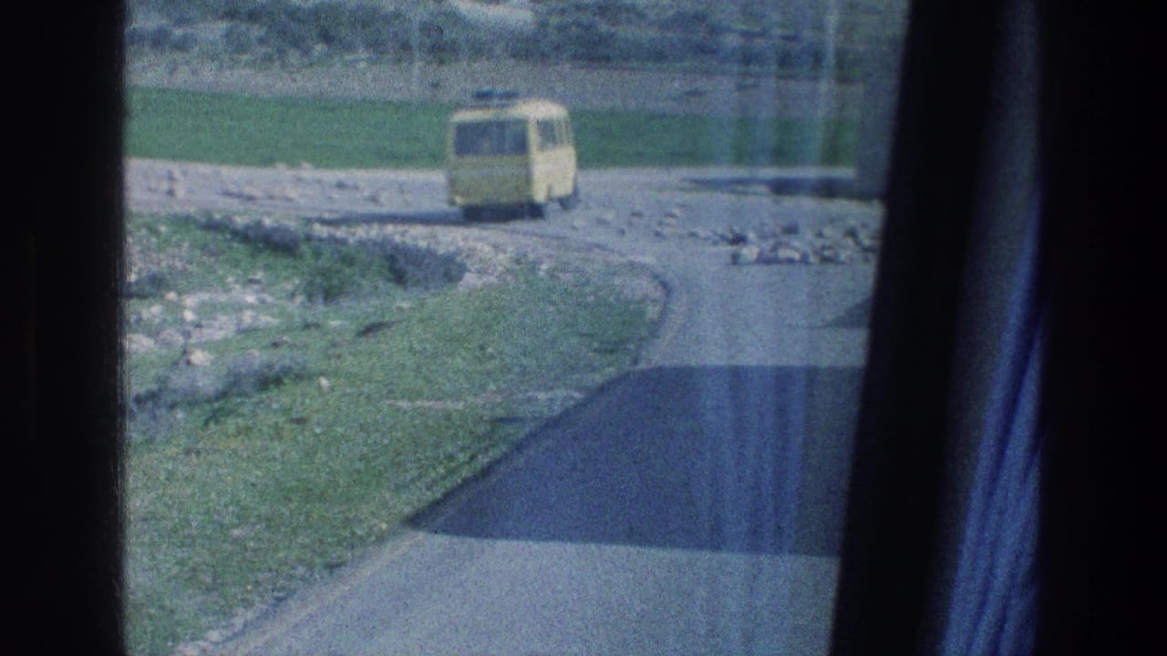 1976 Israel 8mm frame showing a yellow bus moving along a winding rural road, viewed through window glass and curtain edges.