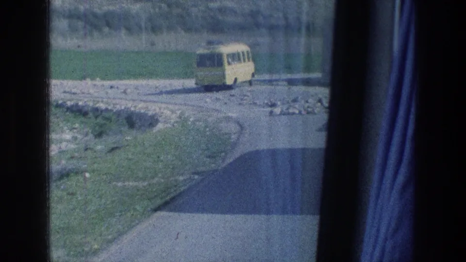 1976 Israel 8mm frame showing the yellow bus passing across a rural road, with curtain framing and film grain visible.