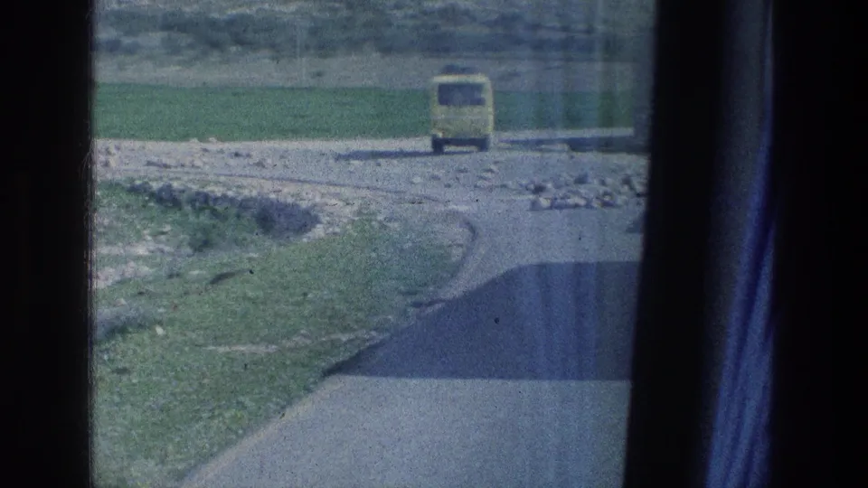 1976 Israel frame showing the yellow bus from behind as it drives away on a winding road through open countryside.