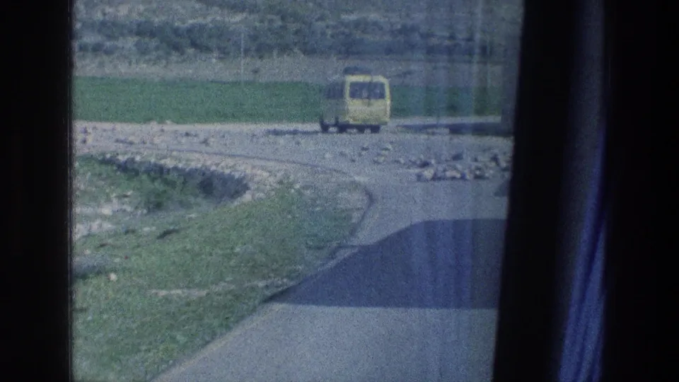 A yellow van travels on a rural road in 1970s Israel, viewed through dark vertical window or film-frame edges.