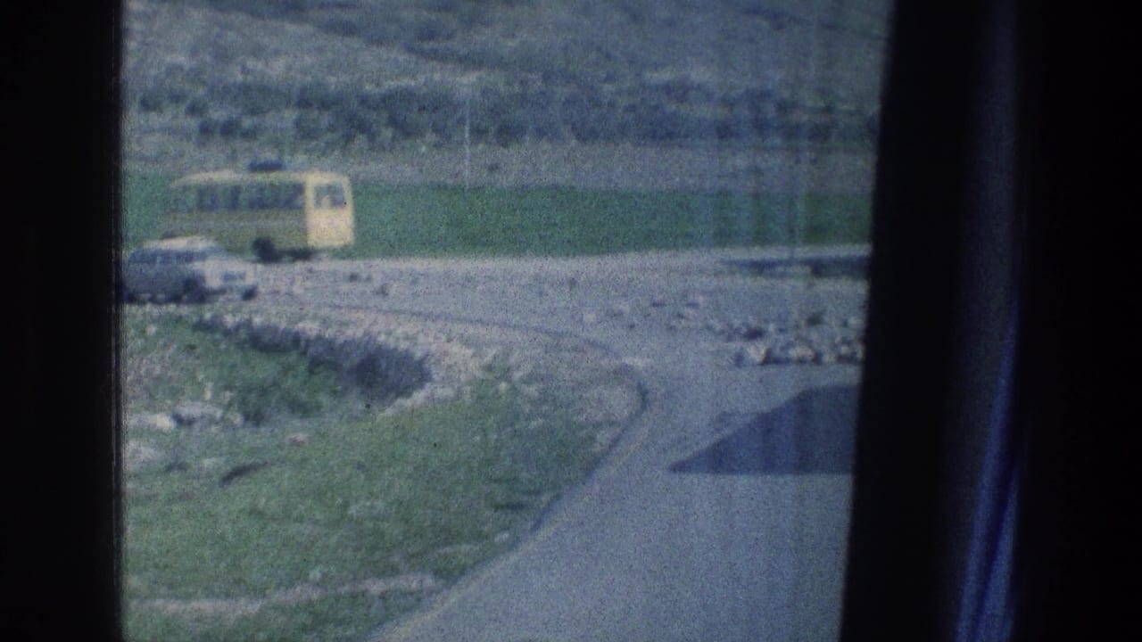 Yellow bus and pale car on a rocky rural road seen through a dark window frame.