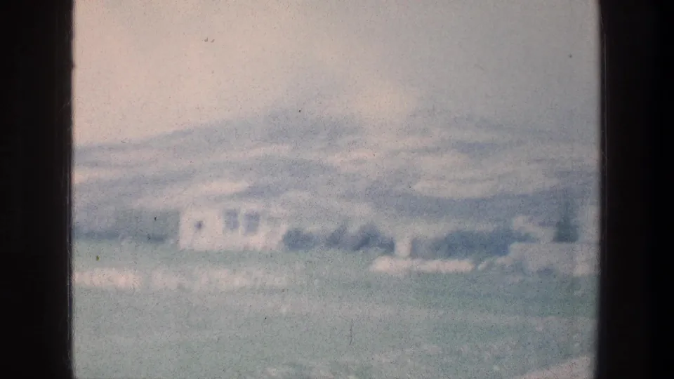 Soft 1976 8mm view across pale rocky terrain toward a distant white building, with faded color and hazy exposure.