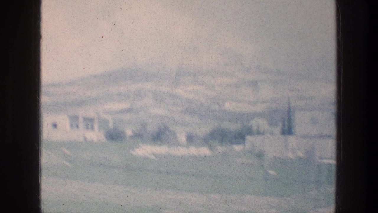 Soft, hazy view across a green field toward pale distant buildings and hills.