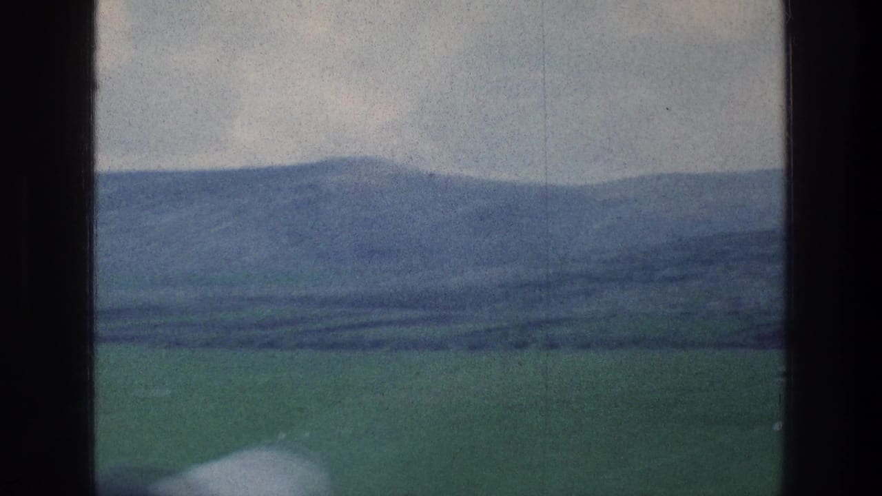 Distant hills and open green fields framed by the vehicle window.