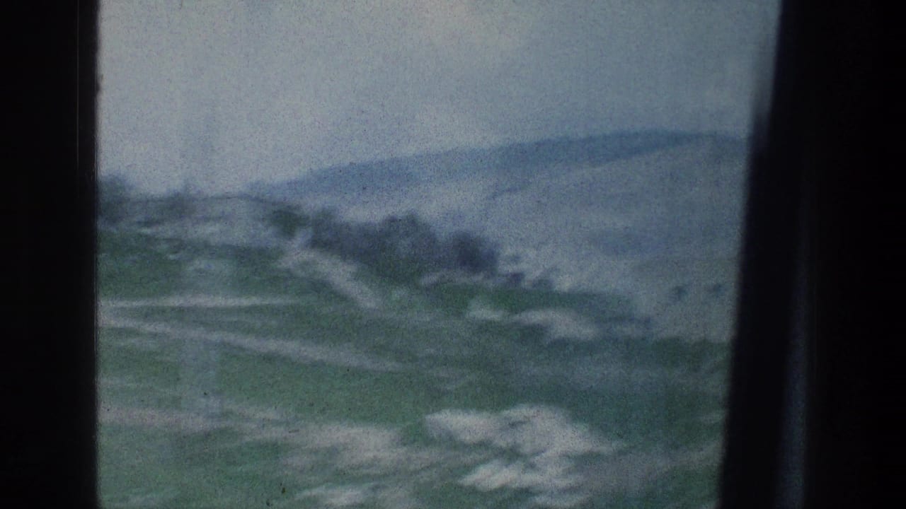 Rolling green hillside seen through a dark car window frame.