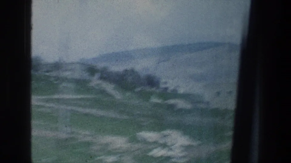 1976 8mm home-movie view from a car window over green hills, roadside ground, and distant slopes in Israel.