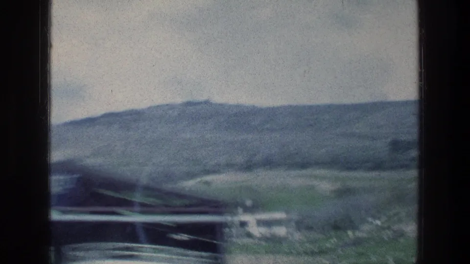Soft 8mm frame of rolling hills and low roadside structures, filmed from a moving car in Israel in 1976.