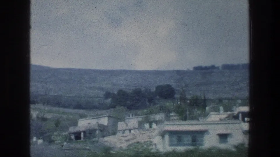 1976 Israel travel frame showing low buildings, trees, and open hills through the vehicle window.