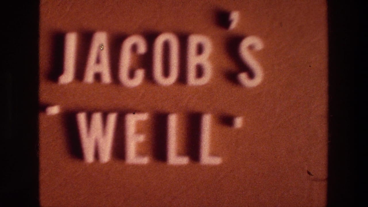 Soft-focus 8mm close-up of a brown Jacob's Well sign with raised white lettering and dark film edges.