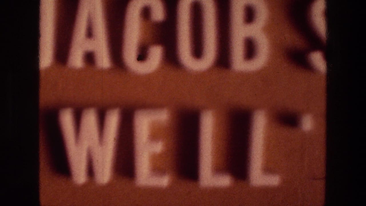 1976 8mm frame from Jerusalem-area travel footage showing a tight, blurred view of the Jacob's Well sign lettering.