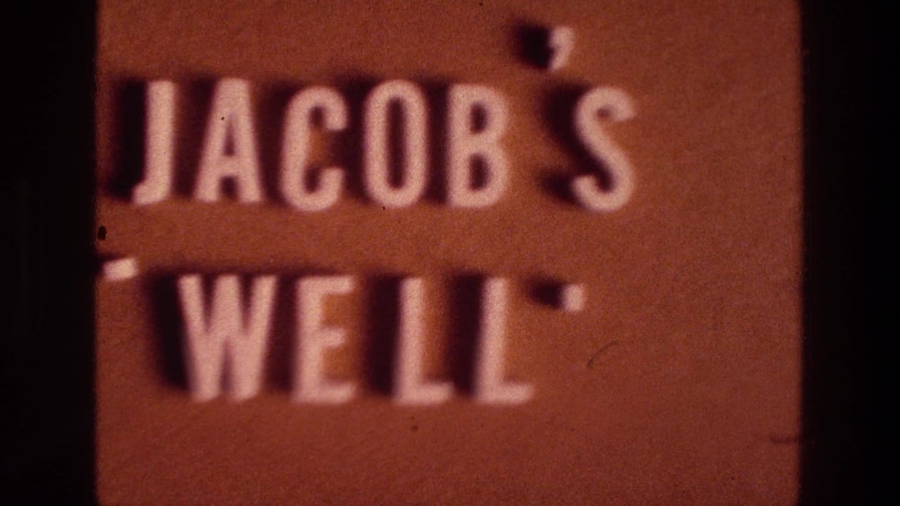 1976 8mm frame showing a reddish Jacob's Well sign partly obscured by the dark edge of a doorway.