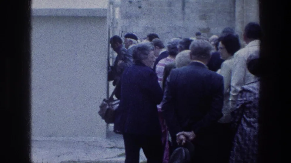 1976 visitor-shot view of adults waiting near a pale wall at Jacob's Well, framed by dark doorway edges.