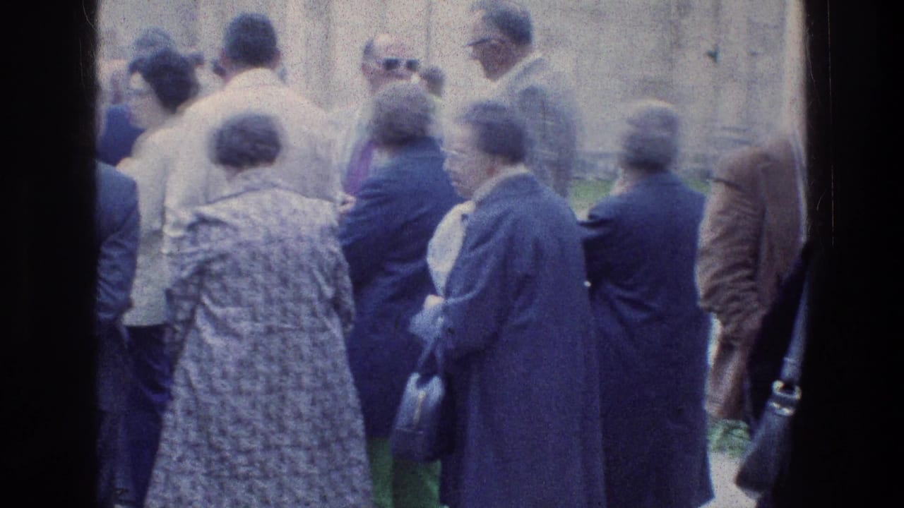 Adults gather near a stone wall, with several people facing away from the camera.