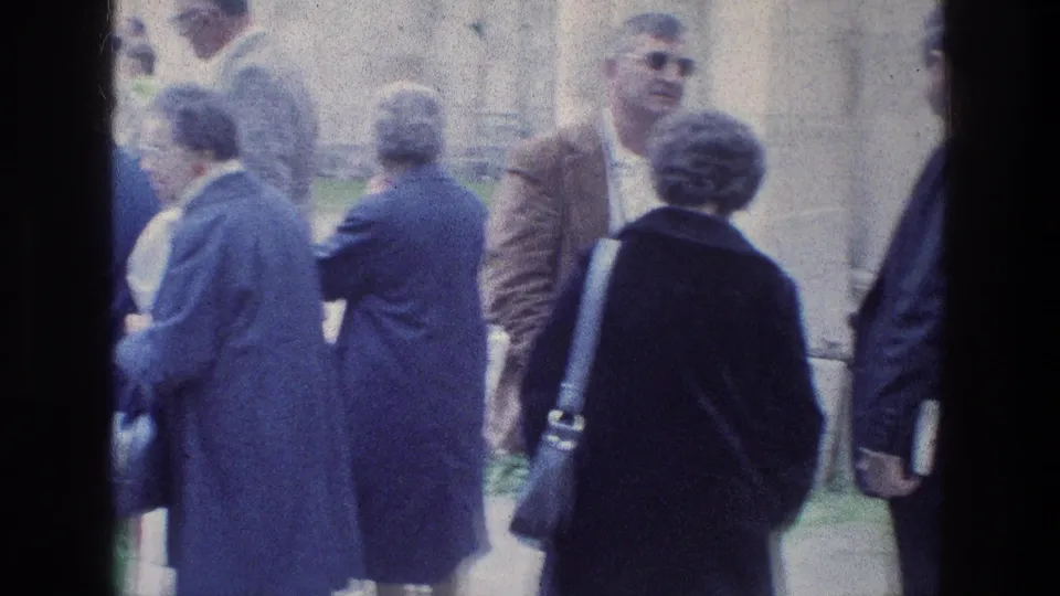 1976 8mm frame at Jacob's Well in Jerusalem with adults in coats and suits standing along a walkway near stonework.