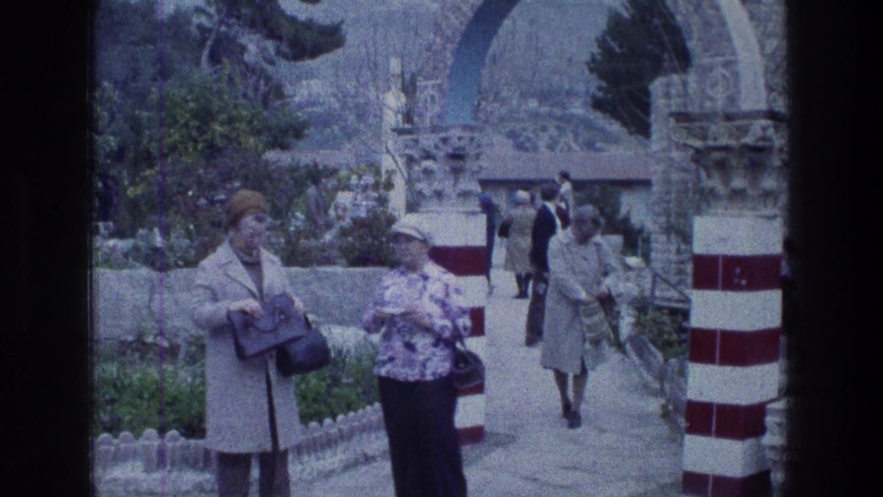 Tourists stand and walk by red-and-white striped columns and a stone archway.
