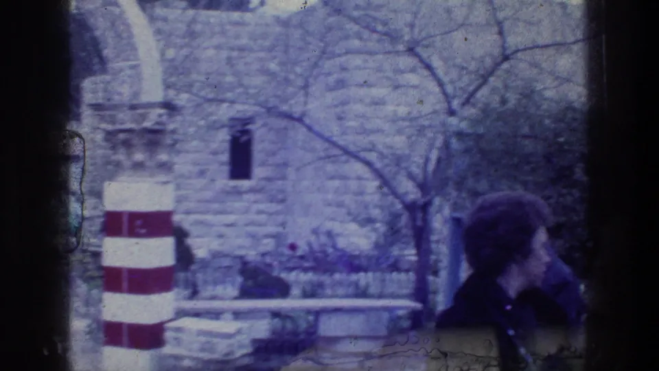 Handheld 8mm view of a visitor near red-and-white striped pillars and stone arches at the Jacob's Well site in Jerusalem.
