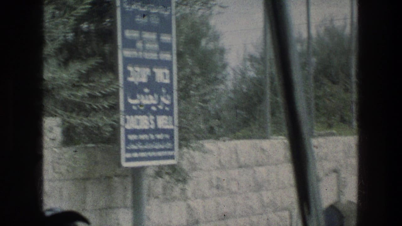 1976 8mm frame at Jacobs Well in Jerusalem, Israel, showing a blue sign near a stone wall through a car window.