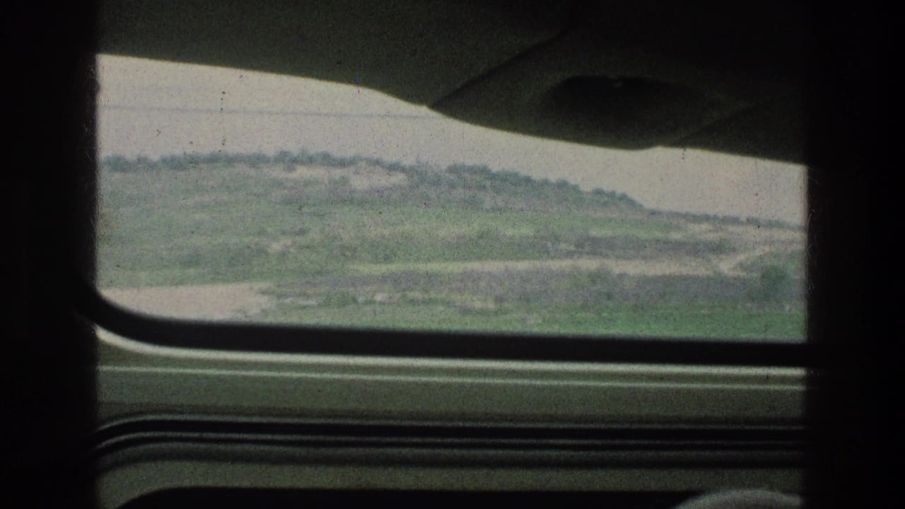 Green hills and pale sky viewed through a car side window.