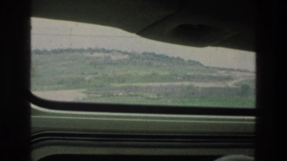 1976 8mm travel frame from Jerusalem, Israel, looking through a car window toward green hills and open terrain.