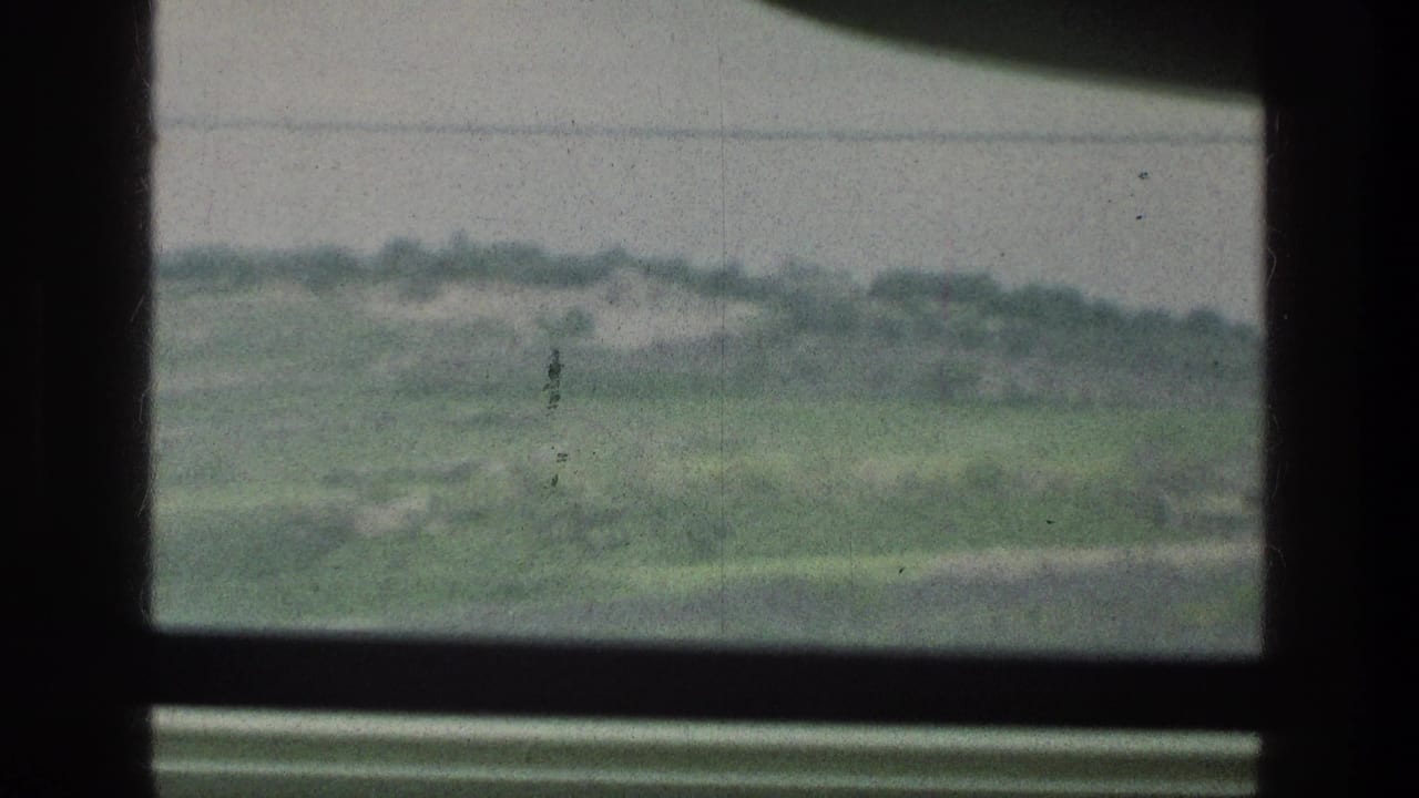 1976 8mm home-movie frame showing green hills and scrub through a dark window frame near the cataloged Jacobs Well Jerusalem Israel location.