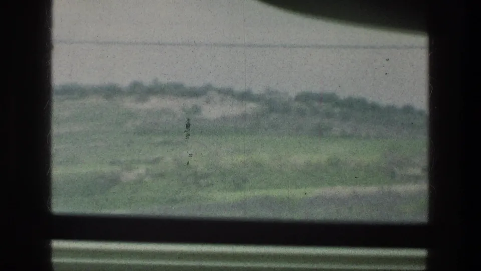 1976 8mm home-movie frame showing green hills and scrub through a dark window frame near the cataloged Jacobs Well Jerusalem Israel location.