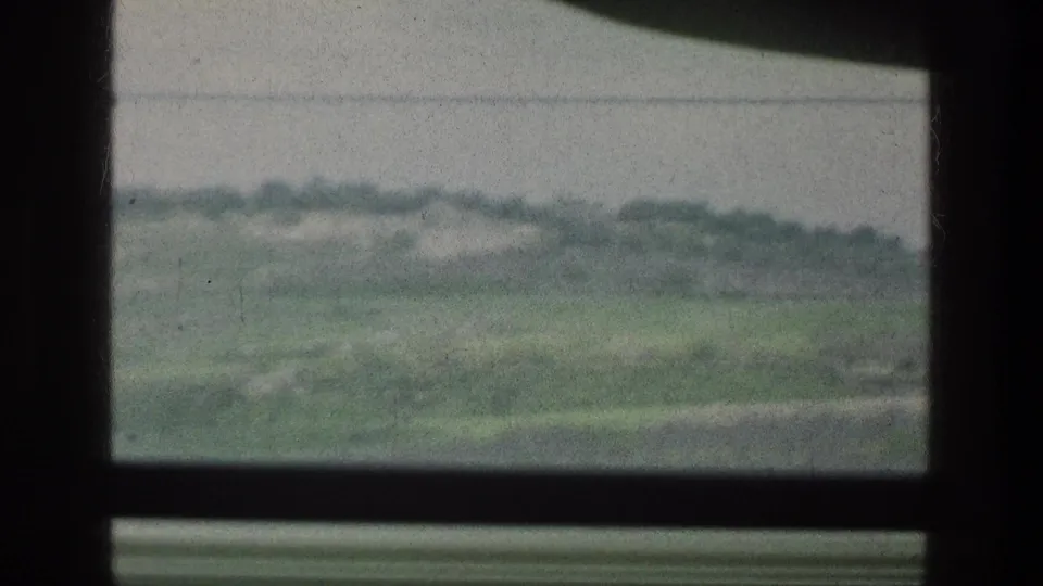 Soft 8mm frame of grassy hills and a pale sky seen through a dark window opening in the 1976 Jacobs Well Jerusalem Israel reel.