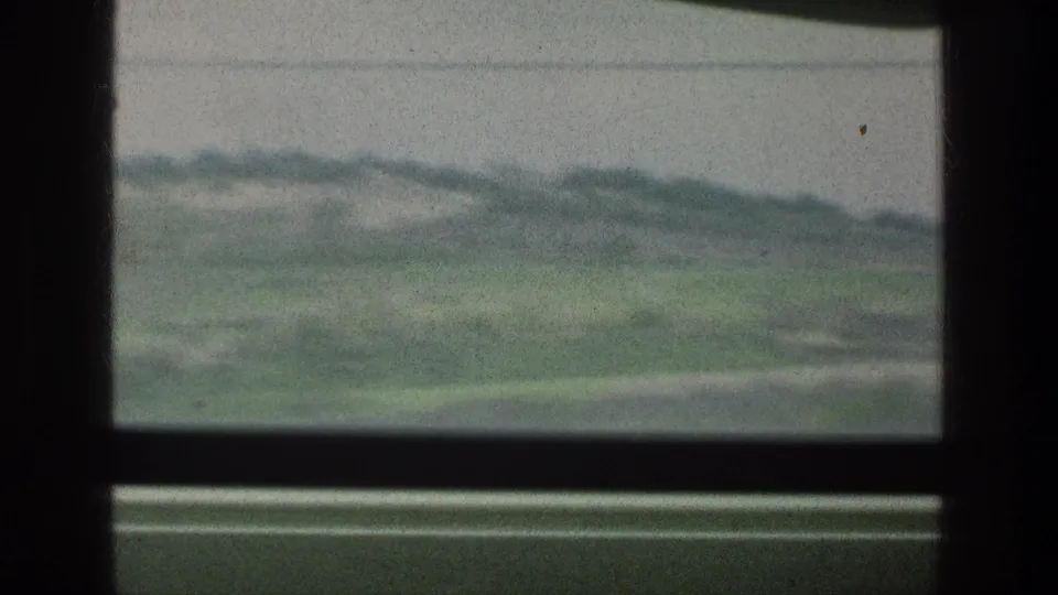 Final 8mm frame of the clip showing green countryside through a window, with dark framing and soft 1970s home-movie texture.