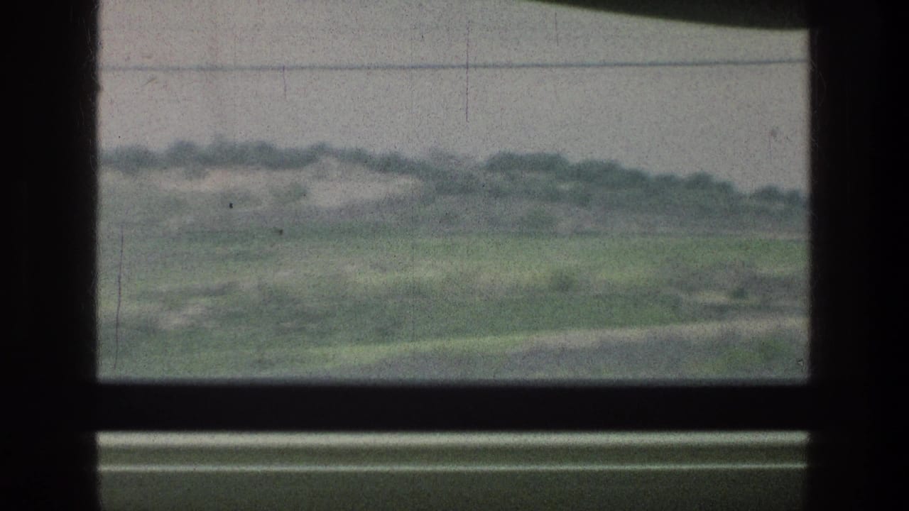 1976 8mm view through a vehicle window toward green fields, distant trees, and an overcast sky near the listed Jerusalem area.