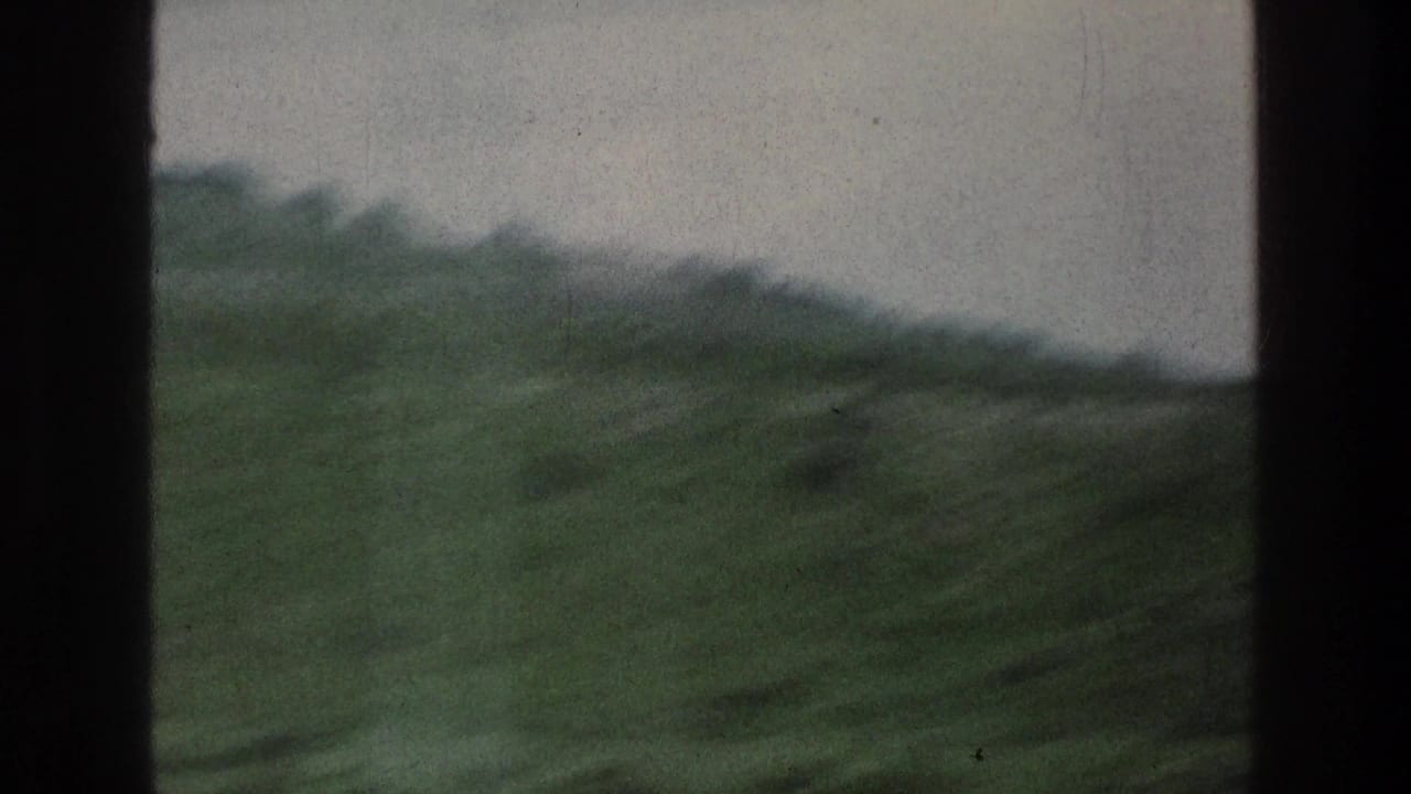 Soft view of green hillside and hazy sky through dark vertical frame edges.